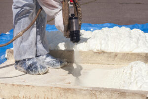 Technician dressed in a protective white uniform spraying foam insulation using Plural Component Spray Gun. Spraying polyurethane foam for roof and energy saving Roofing Contractors in Macomb IL