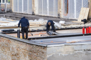 Roofing Contractors Moline IL 2 Two workers from Big River Roofing, roofing contractors in Moline IL, install a black waterproofing membrane