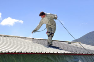 A trademan from Big River Roofing, roofing contractors Peoria IL and roofing contractors Muscatine IA trusts, uses an airless spray to paint the roof of a building